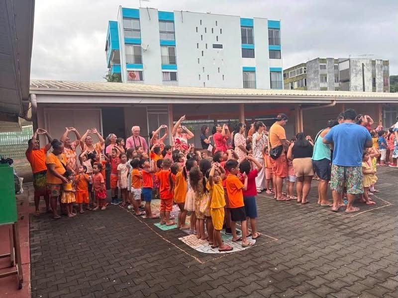 Enfants et adultes en orange dans la cour de l'école, bras levés