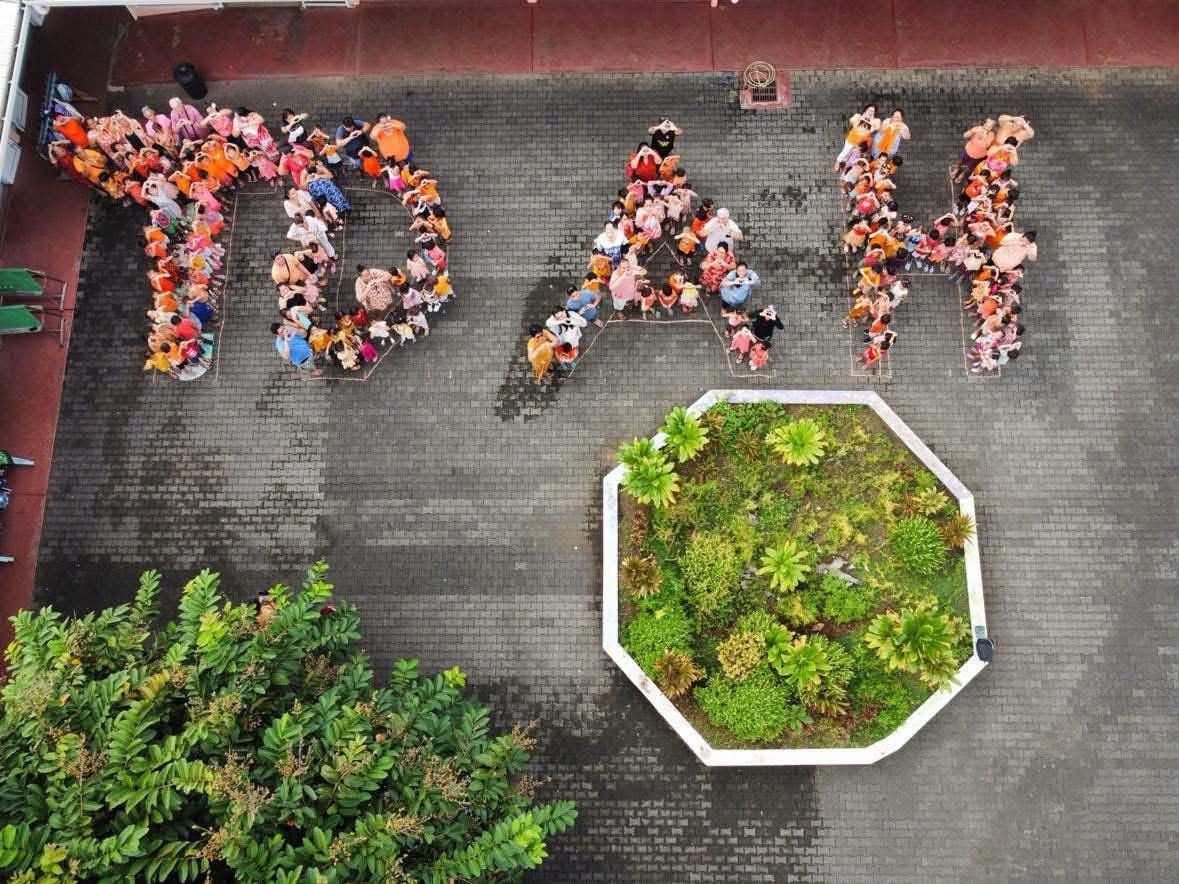 Vue du ciel : enfants, parents et enseignants vêtus d'orange forment les lettres TDAH dans une cour d'école