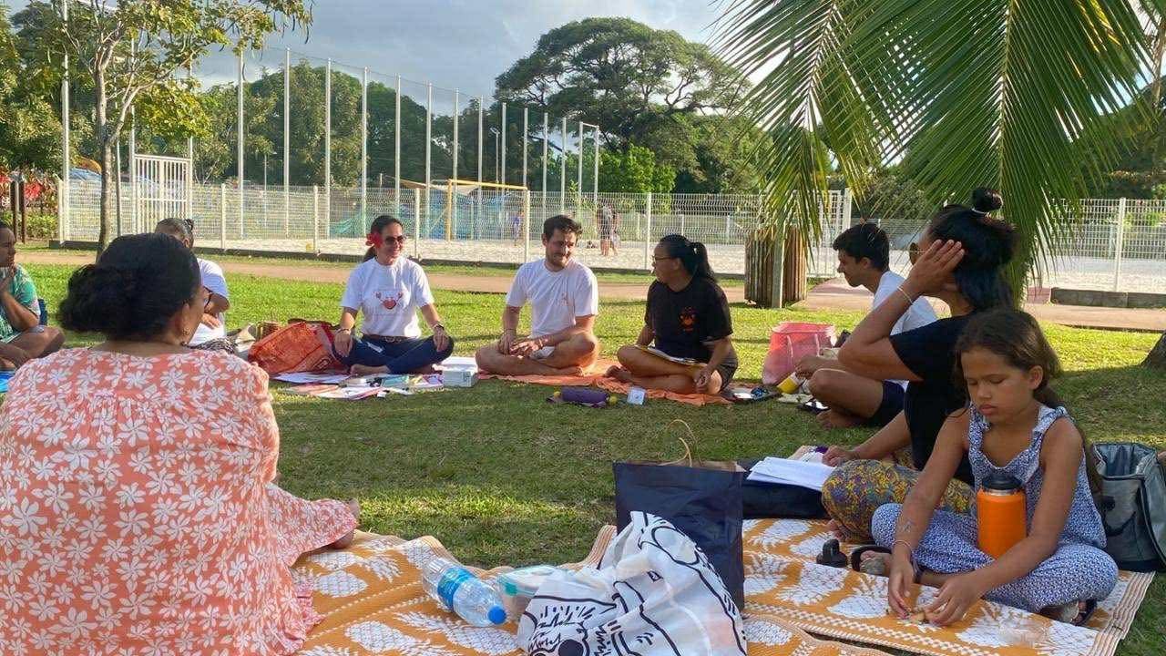 Parents et professionnels assis en cercle sur des nattes dans l'herbe