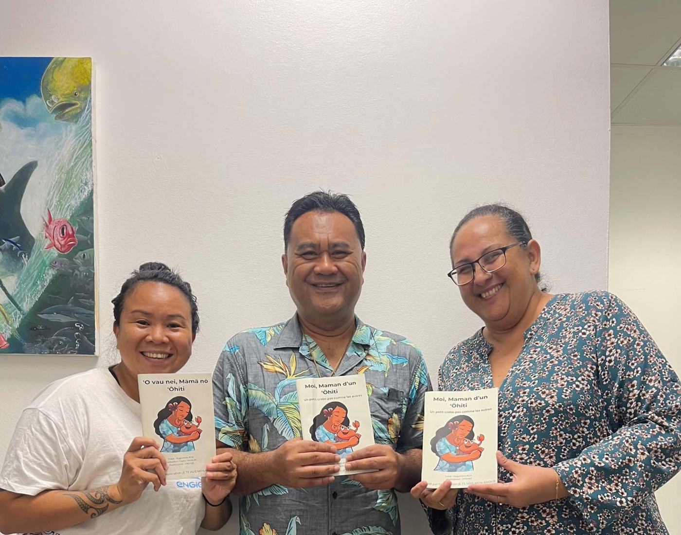 Trois personnes souriantes tenant le livre en français et en Reo ma'ohi